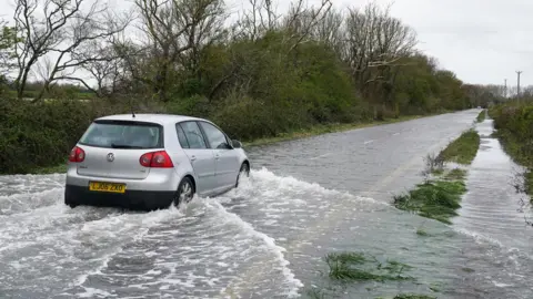 Gareth Fuller/PA Wire Car drives through flood water in Littlehampton, West Sussex