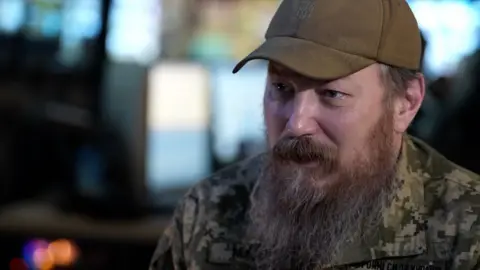 Unmanned Systems Forces commander Robert Brovdi, wearing a cap and with a long beard, is pictured speaking to the BBC