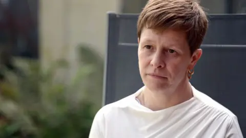 A headshot of Samantha Billingham. She is sitting outside in a garden chair. She is wearing a white top and is looking at someone who is interviewing her.