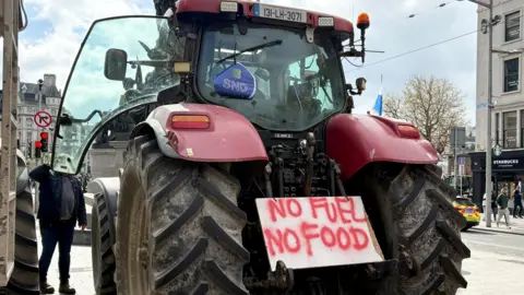 A large red tractor from behind - a white placard with red paint sits between the back wheels. The paint reads "No fuel no food". The tractor sits in O'Connell Street in Dublin.