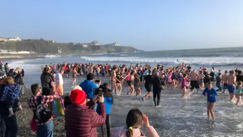 Hundreds of people running into the sea, you can see Onchan Head in the background.