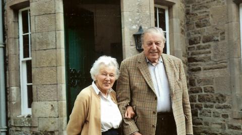 Cherry Palmer, left, and Bill Palmer, right. Cherry is wearing a light brown cardigan, chequered skirt and white blouse, and Bill is wearing a patterned jacket, dark trousers and white shirt