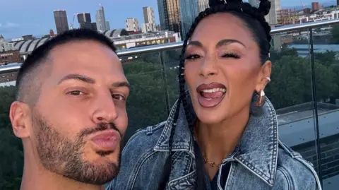 Carl Bembridge Carl Bembridge poses with the singer Nicole Scherzinger from The Pussycat Dolls. Nicole wears a denim jacket and in the background is a city skyline