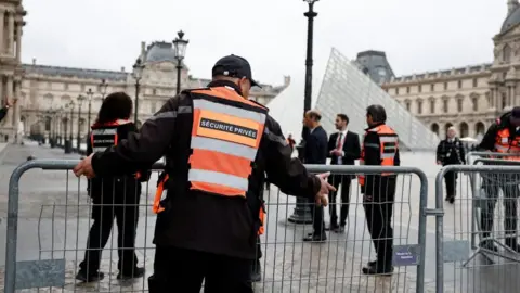 A security guard helps to put up a metal barrier infront of the Louvre pyramid entrance