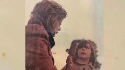 Family handout A woman wearing a red coat looking down whilst her child with brown hair and a brown coat, who is holding an ice-cream is looking at up at her