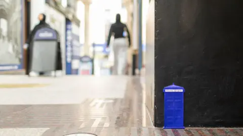 James Beck A miniature blue Police Box that has been attached to a wall's corner by the ground in St Nicks Market in Bristol. It's reminiscent of the Dr Who police box.