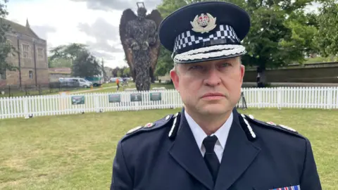 John Devine/BBC Police officer in senior uniform with epaulettes stands on a lawn with Knife Angel in the background