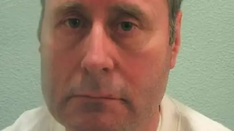 Met Police A mugshot of John Worboys. He is staring into the camera, and wearing a white top.