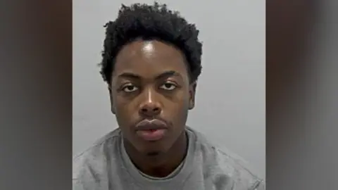 Bedfordshire Police Bennett Ndenkeh: The head and shoulders of a man with black hair wearing a grey round-necked top.
