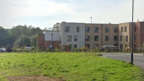 A red brick building with lots of windows is situated next to a road. 