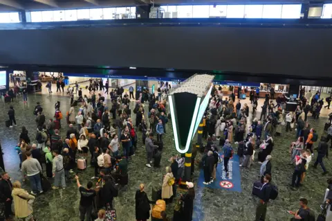 PA Media Above the concourse, a long black strip above passengers gaze up at a smaller departures board 