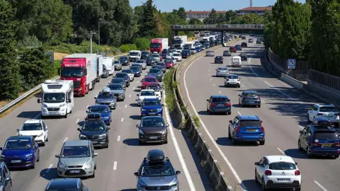 Getty Images Cars and trucks are stuck one behind the other at a stop, forming a traffic jam on the three lanes of the A7 motorway in the North South direction, class Red by Bison Fute, near Bourg les Valence, France, July 5, 2025. 