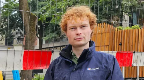 Jamie Osborn standing next to a fence. He's wearing a blue Berghaus jacket over a green shirt