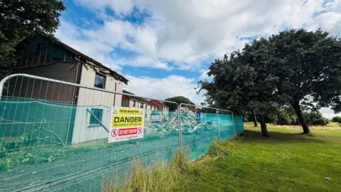 Demolished houses in Aberdeen, due to the presence of potentially dangerous concrete, with a fence outside and danger warning sign.