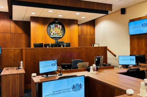 The interior of the civil annexe of Aberdeen Sheriff Court, with computer screens and a court emblem.