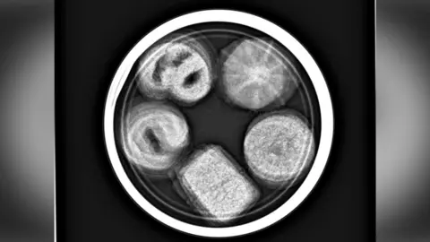 Contributed A round tin of biscuits with biscuits inside is pictured as a black and white X-ray.