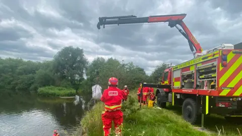 Derbyshire Fire and Rescue Service A fire truck with an over head beam, pulling a sheep in a white bag out of the river