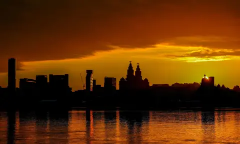 The sun rises behind Liverpool's skyline with the River Mersey out in front