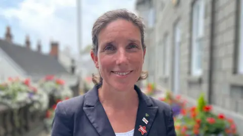 Deputy Lindsay de Sausmarez, who is wearing a suit, smiles at the camera.