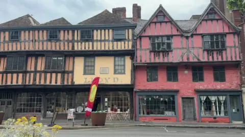A historic street showing timber Tudor framed houses and shops with mullioned windows.