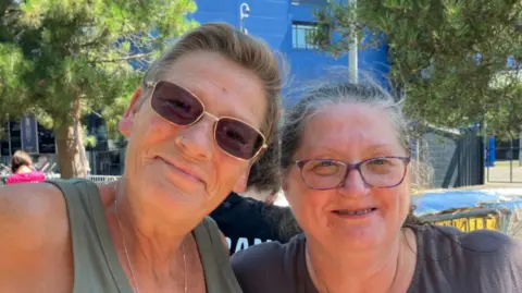 Alice Cunningham/BBC Tina Hoff and Linda Kennedy stand together and smile at the camera. Tina has short hair and wears sunglasses. Linda has long grey hair that is tied up and she wears glasses.