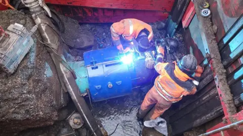 Welsh Water Engineers in orange jackets are seen fixing a pipe