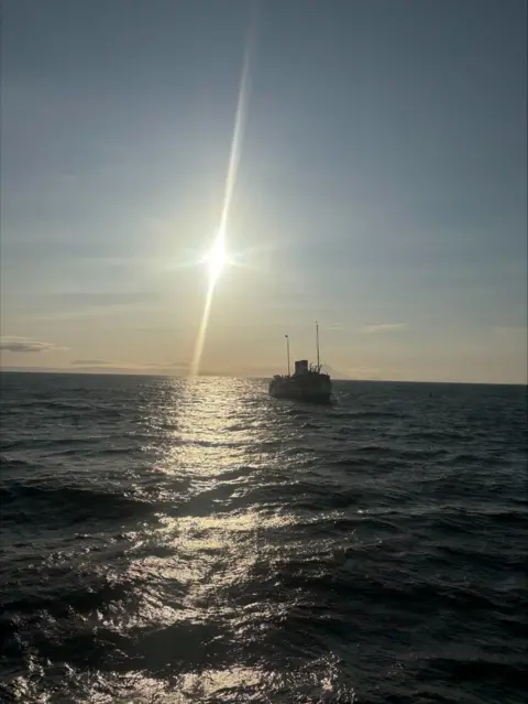 Jordan Cunningham A boat silhouetted with the sun in the background. The water is choppy.