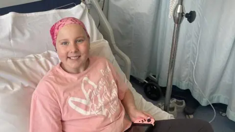 Eve Shipley receiving hospital treatment. She is wearing a pink shirt with a white heart and white lettering over the top. She has a pink scarf over the top of her head.