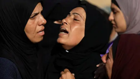 Palestinian women mourn at the funeral of people who were killed while seeking aid in northern Gaza, at al-Shifa hospital, Gaza City (18 June 2025)