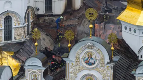 Ukrainian firefighters work at the roof of the damaged Dormition Cathedral 