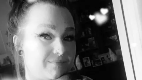 Family picture A black and white photograph shows Simone looking at the camera and smiling. She has her hair in a ponytail and piercings to her nose and ear.