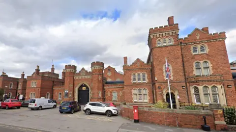 Google The outside of HMP Lincoln. There are cars parked and a red post box in front of the building.