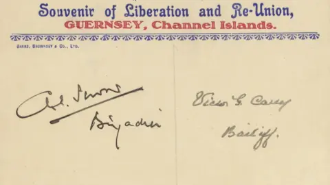 Mark Lamerton Collection An old postcard. The text is printed in blue and red and there are two signatures on the card.  The text says "Souvenir of Liberation and Re-Union" and this is followed by "Guernsey, Channel Islands".