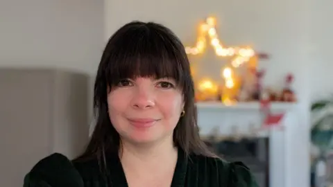 TRISH MCDONNOUGH Trish, a woman with brown hair and a fringe, smiles for the camera. She is wearing a black top.