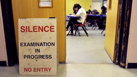 An exam hall with a sign. Sign read 'SILENCE. Examination in progress. NO ENTRY'