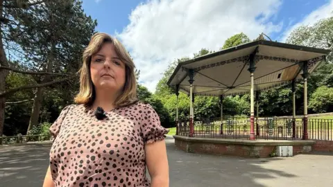 Councillor Fiona Torbin near the bandstand at Barnes Park. She is wearing a pale pink t-shirt with black dots. Her blonde reaches just past her shoulders and is parted in the middle.