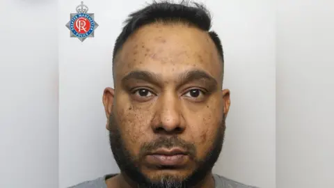GMP A police mugshot of Rawal Rehman, who has a short beard and black hair cropped at the sides and longer on top. He stares into the camera with a blank expression. 