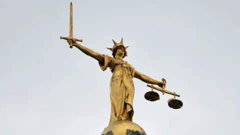 Golden statue of Justice on top of the Old Bailey, with scales of justice in one had and a sword on the other. She has a crown on her head.