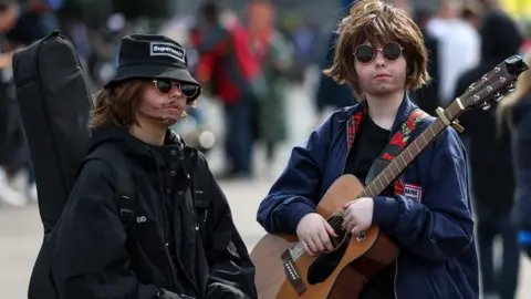 Getty Images Two children dressed as Liam and Noel Gallagher. One has a guitar in a case on his back while the other has one over his shoulder. They both have fake stubble and are wearing sunglasses. One is wearing a black bucket hat with "Supersonic" on it.