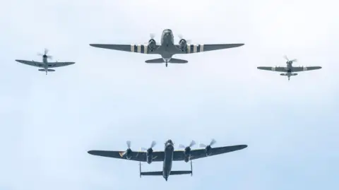 Silhouettes of four aircraft, two large two small on a pale blue sky. The largest aircraft has four rotors.