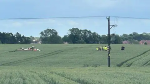 Emergency workers can be seen in a field where an aircraft has crashed.