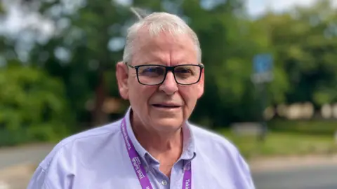 Martin Giles/BBC Andrew Smith is looking at the camera and is wearing a pale blue shirt. He has short, grey hair and is wearing spectacles.