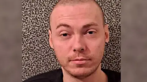 Police Scotland Grant McKinnon is looking straight at the camera. He has a shaved head and is wearing a black top