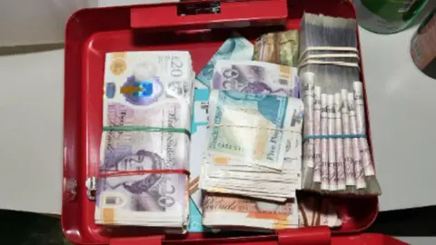 GMP Wads of cash tied up in elastic bands are seen stashed in a red container