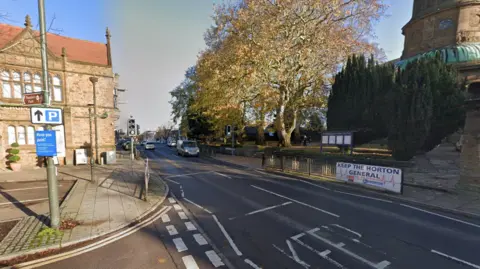 A general view of North Bar Street, a two-lane carriageway with traffic lights. St Mary the Virgin Church is on the far side of the picture.