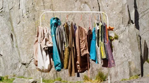 Jess O'Riley A clothes rail in front of a rock wall, with Jess' items on display which include several bright pieces of clothing.