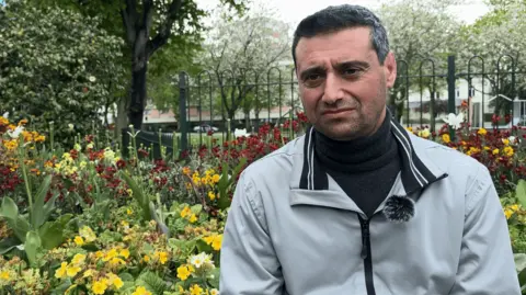 A man in a grey jacket sits in front of a play area.