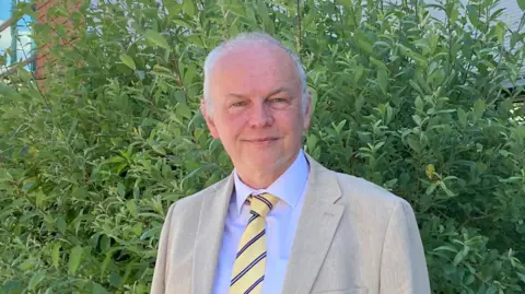 Profile picture of Mark Argent in beige suit and yellow tie with stripes