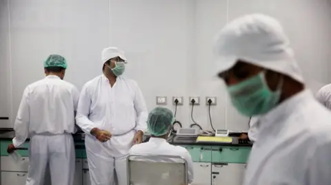 Getty Images Obraz pokazuje pracowników pracujących w laboratorium w Laurus Labs Ltd. Pracy farmaceutyczne w Visakhapatnam, Andhra Pradesh, Indie, noszące białe kurtki i maski.