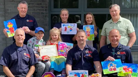 ECFRS Olive, her brother Freddie and firefighters at Rayleigh Weir are all posing with paintings she has made.